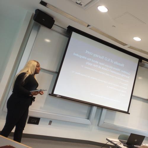 [a student stands in front of projected slides delivering a symposium presentation]